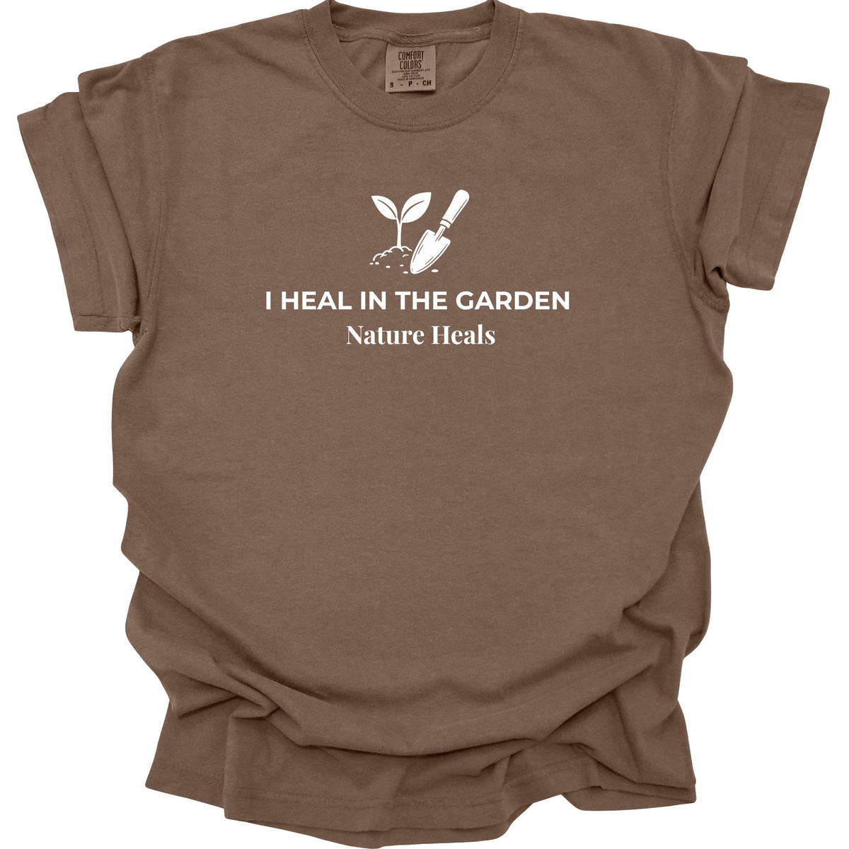 An espresso-brown short-sleeve t-shirt with a white graphic print of a sprout, trowel, and the text 'I HEAL IN THE GARDEN Nature Heals' on the chest, displayed on a clean white background.
