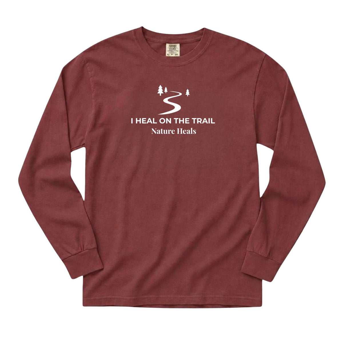 A long-sleeve crewneck t-shirt in brick red, featuring a white graphic print on the chest with the text 'I HEAL ON THE TRAIL Nature Heals' and a stylized trail design.