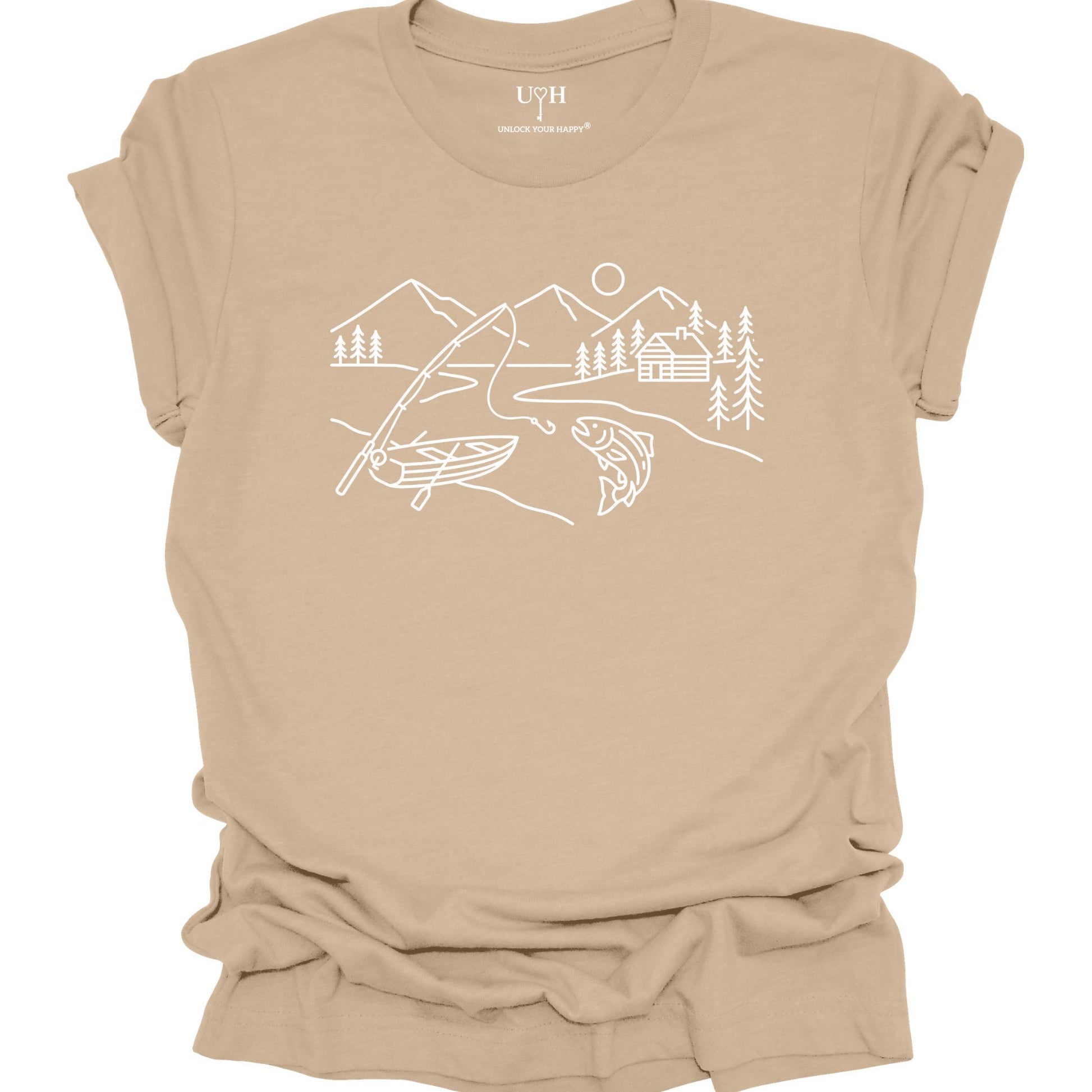 Tan t-shirt featuring a minimalist white line art fishing design with mountains, river, canoe, fish, cabin, and pine trees.
