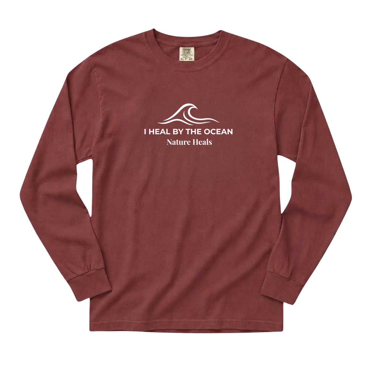 A brick red colored long-sleeve t-shirt with a white graphic on the chest showing an ocean wave and the text 'I HEAL BY THE OCEAN  Nature Heals'.