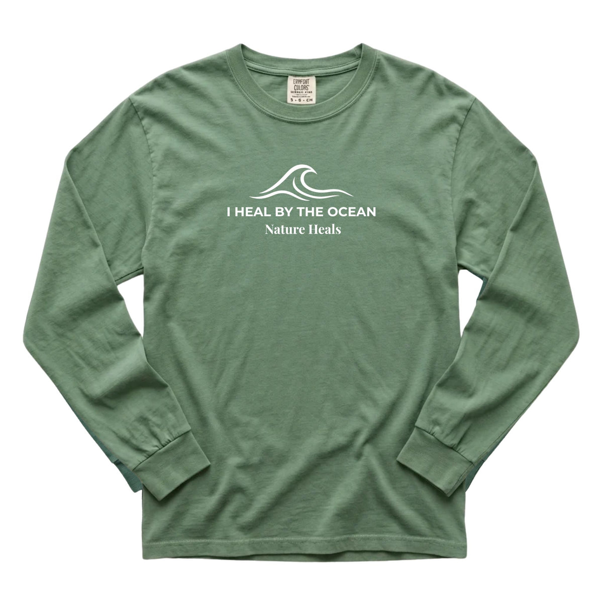 A green long-sleeve t-shirt with a white graphic on the chest showing an ocean wave and the text 'I HEAL BY THE OCEAN  Nature Heals'.