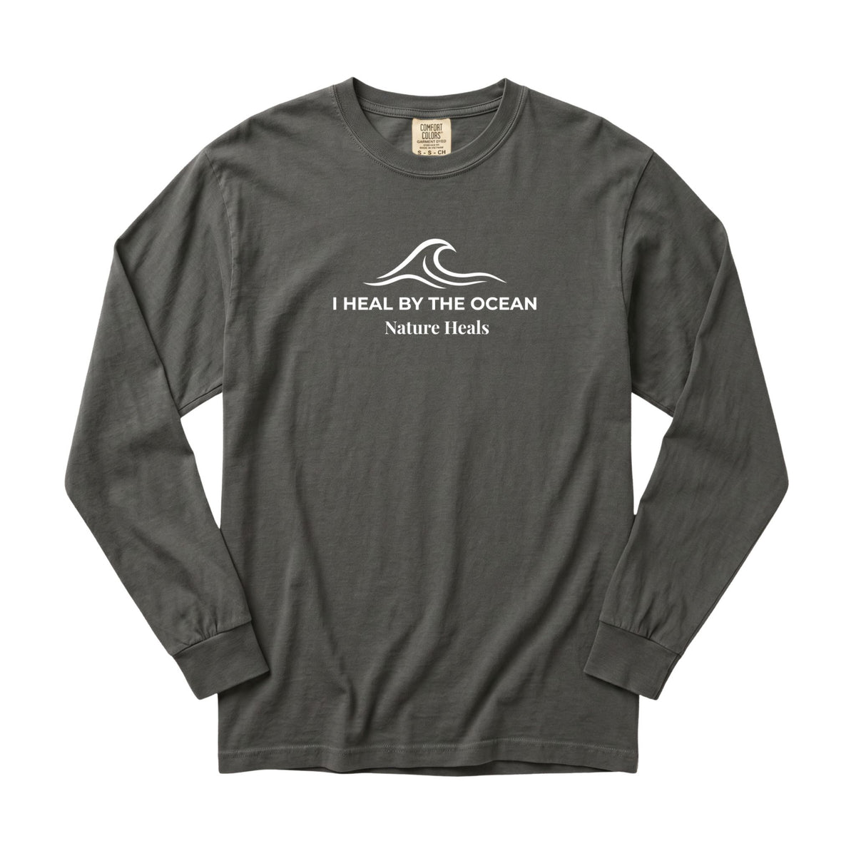 A pepper-gray long-sleeve t-shirt with a white graphic on the chest showing an ocean wave and the text 'I HEAL BY THE OCEAN  Nature Heals'.