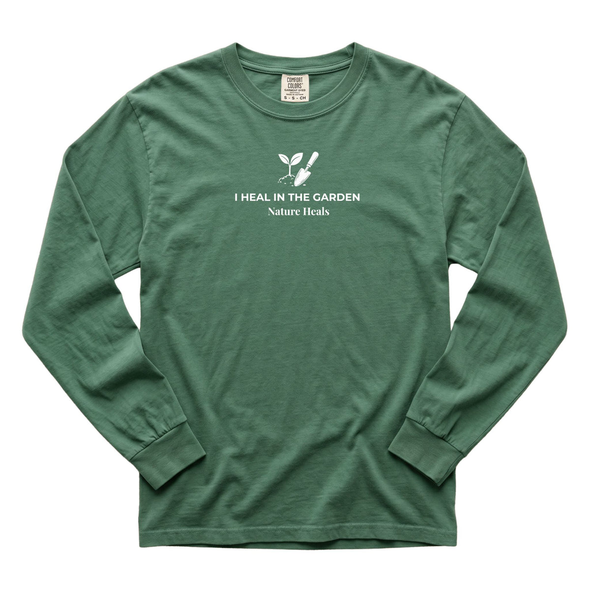 A  blue spruce green colored long-sleeve t-shirt with a white graphic on the chest showing a mound of soil, plant and trowel  and the text 'I HEAL IN THE GARDEN  Nature Heals'.
