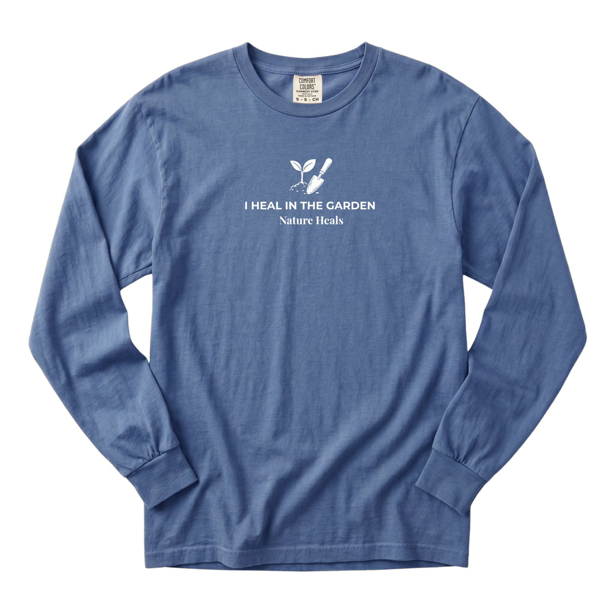 A blue long-sleeve t-shirt with a white graphic on the chest showing a mound of soil, plant and trowel  and the text 'I HEAL IN THE GARDEN  Nature Heals'.