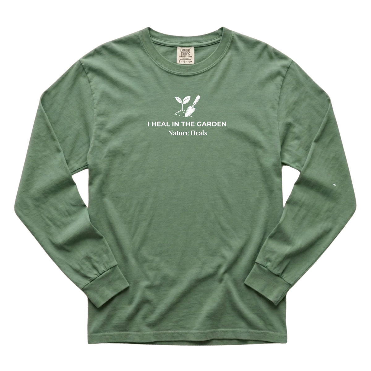 A light-green long-sleeve t-shirt with a white graphic on the chest showing a mound of soil, plant and trowel  and the text 'I HEAL IN THE GARDEN  Nature Heals'.