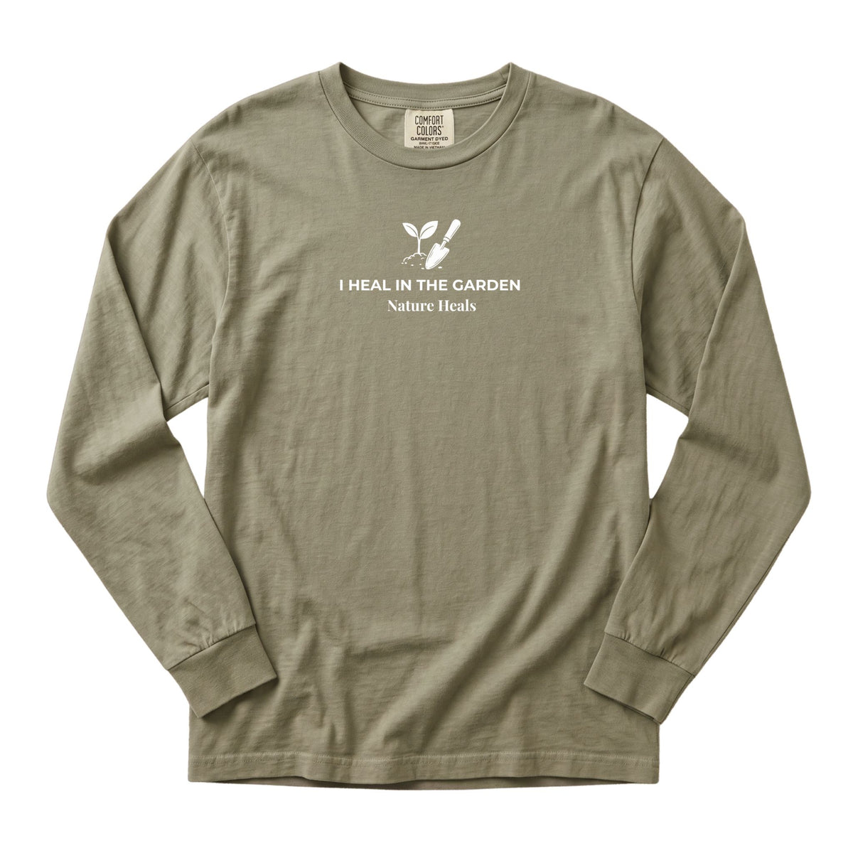 A sandstone long-sleeve t-shirt with a white graphic on the chest showing a mound of soil, plant and trowel  and the text 'I HEAL IN THE GARDEN  Nature Heals'.