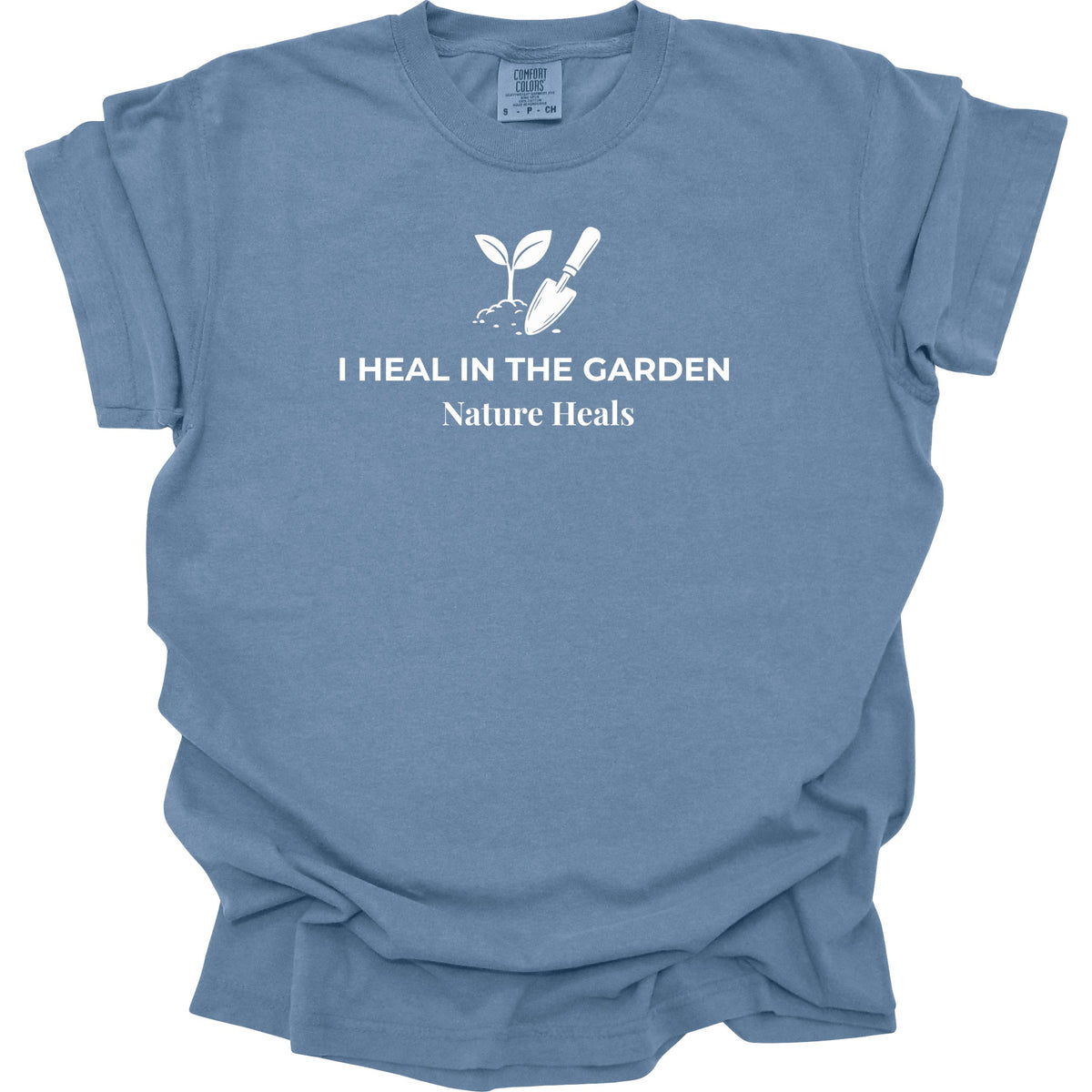 A blue t-shirt with a white graphic of a sprout and trowel and the text 'I HEAL IN THE GARDEN' and 'Nature Heals' printed on the chest, displayed on a clean white background.
