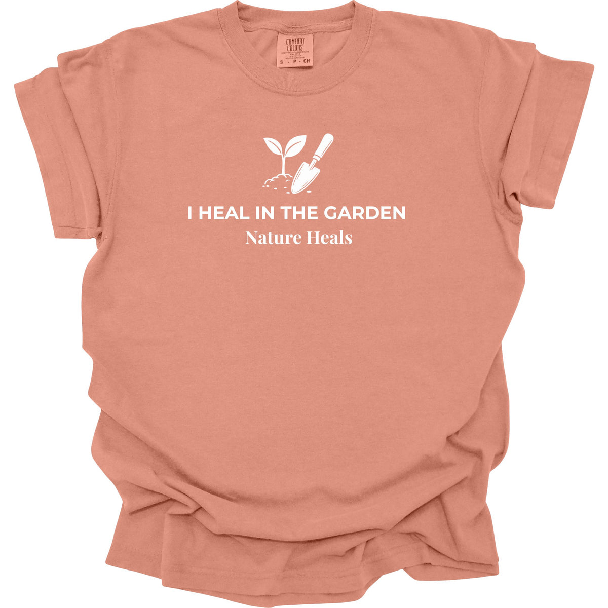 A terracotta-colored crewneck t-shirt with a white graphic of a sprout and gardening tools, accompanied by the text 'I HEAL IN THE GARDEN' and 'Nature Heals'.