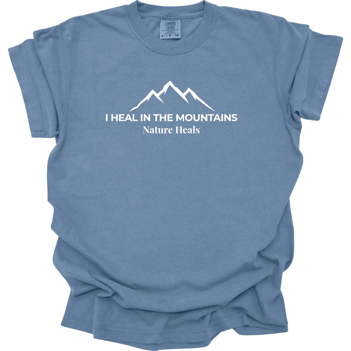A blue colored short-sleeve t-shirt with a white graphic of a mountain range and the text 'I HEAL IN THE MOUNTAINS Nature Heals' printed on the chest, displayed against a solid white background.