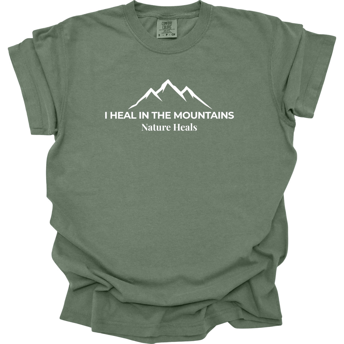 A moss-green colored short-sleeve t-shirt with a white graphic of a mountain range and the text 'I HEAL IN THE MOUNTAINS Nature Heals' printed on the chest, displayed against a solid white background.