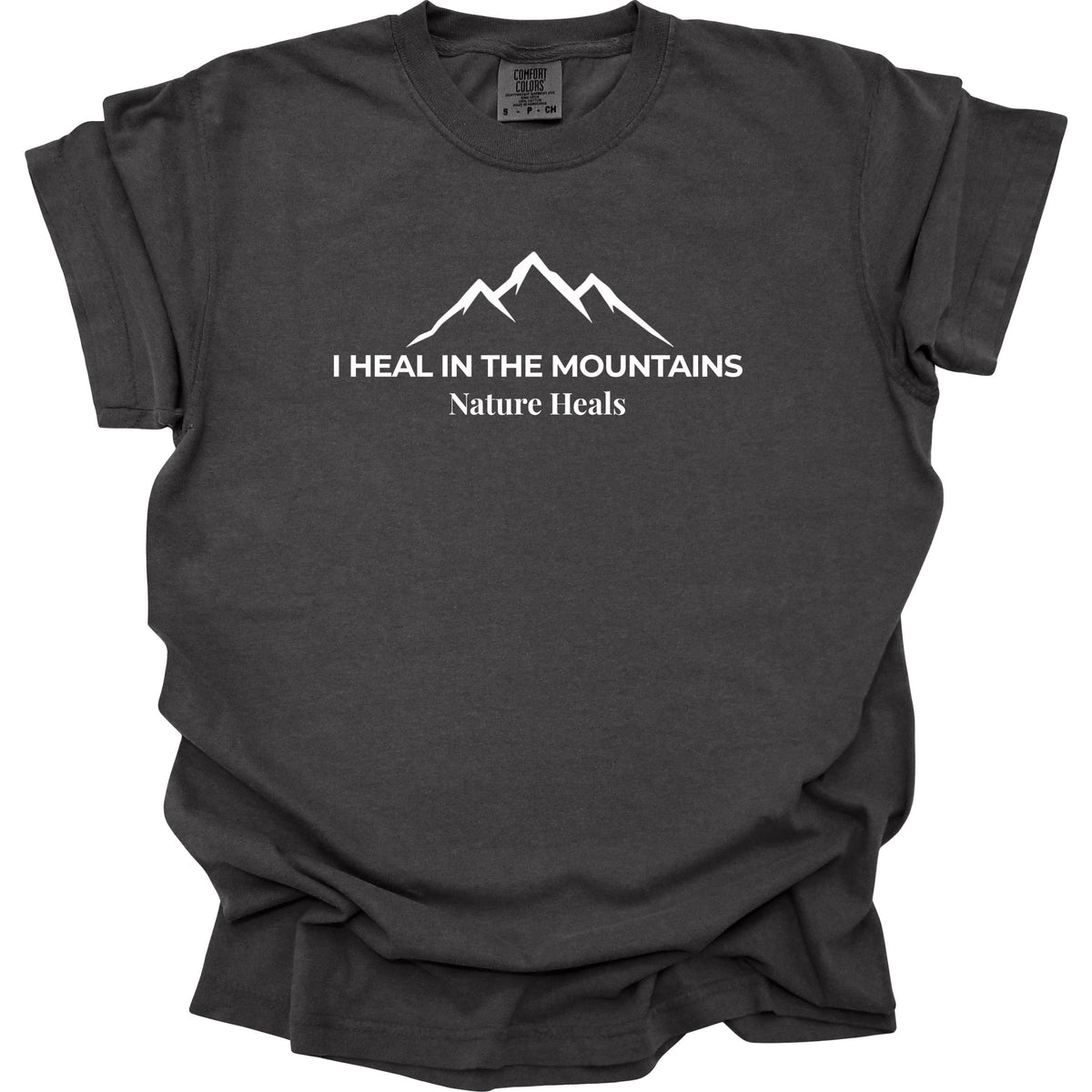 A pepper-grey colored short-sleeve t-shirt with a white graphic of a mountain range and the text 'I HEAL IN THE MOUNTAINS Nature Heals' printed on the chest, displayed against a solid white background.