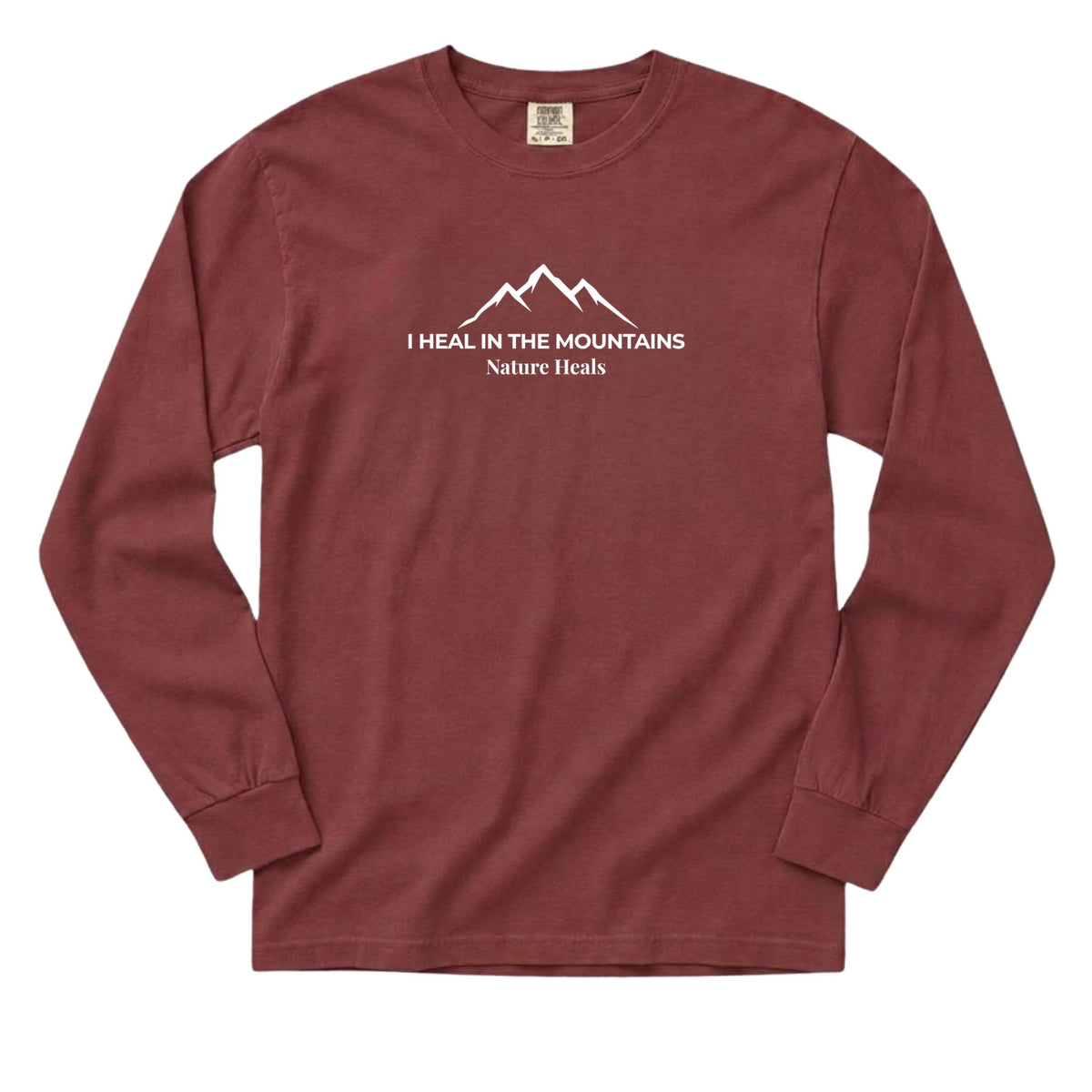 A long-sleeve crewneck t-shirt in a dusty brick red color, featuring a white graphic of three mountains and the text 'I HEAL IN THE MOUNTAINS Nature Heals' printed on the chest.