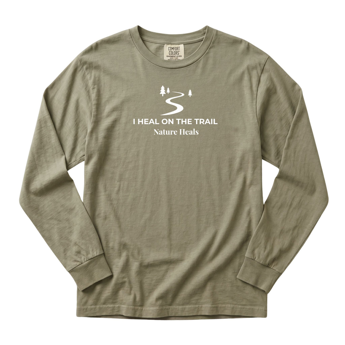 An sandstone colored long-sleeve t-shirt with a white graphic print on the chest that reads 'I HEAL ON THE TRAIL Nature Heals' with a winding trail and trees, displayed on a clean white background.