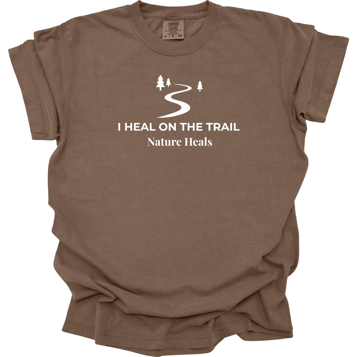 A brown t-shirt featuring white text that reads 'I HEAL ON THE TRAIL Nature Heals' and a trail icon graphic, with a white background.