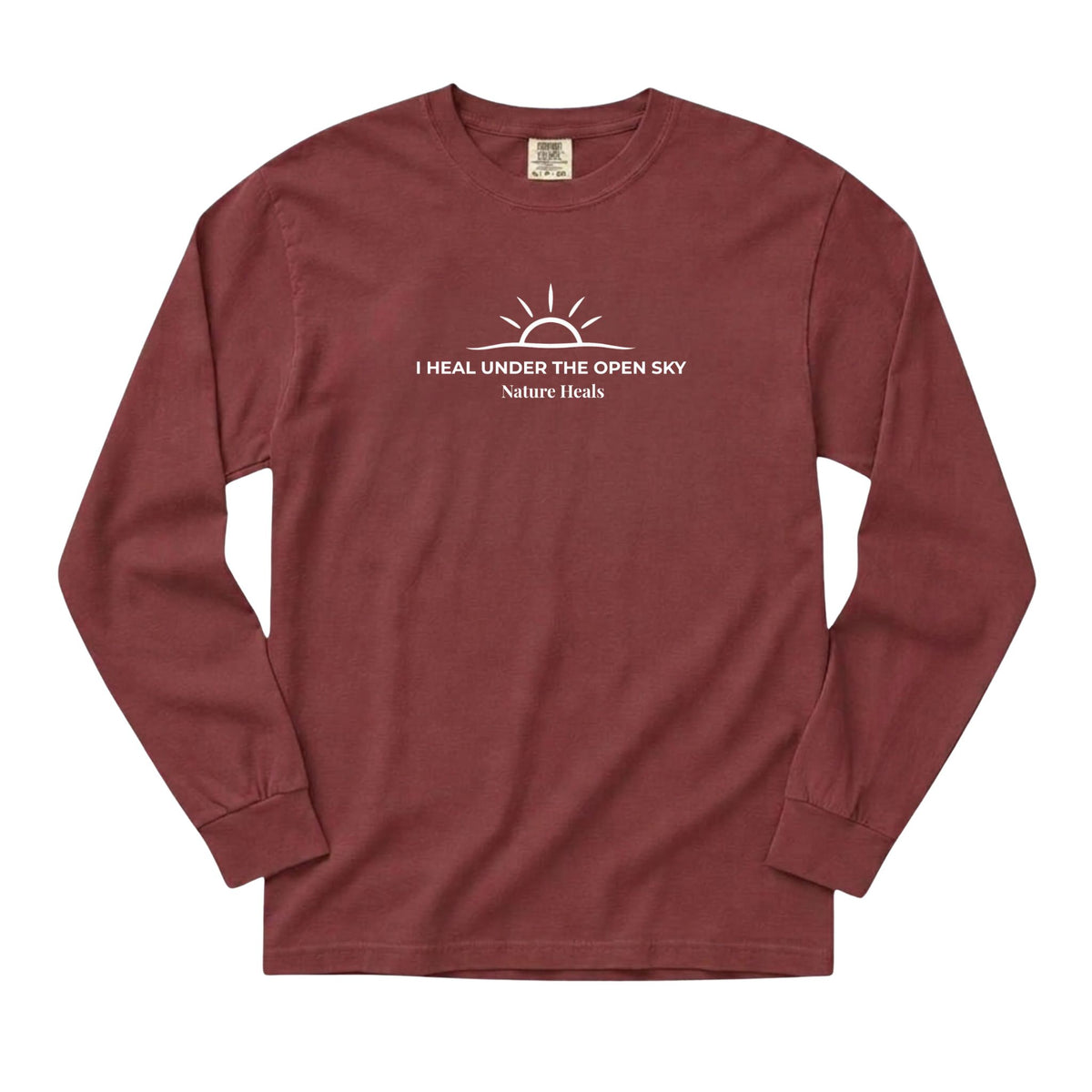 A long-sleeve crewneck t-shirt in brick red with a white graphic on the chest showing a sun and the text 'I HEAL UNDER THE OPEN SKY Nature Heals'.