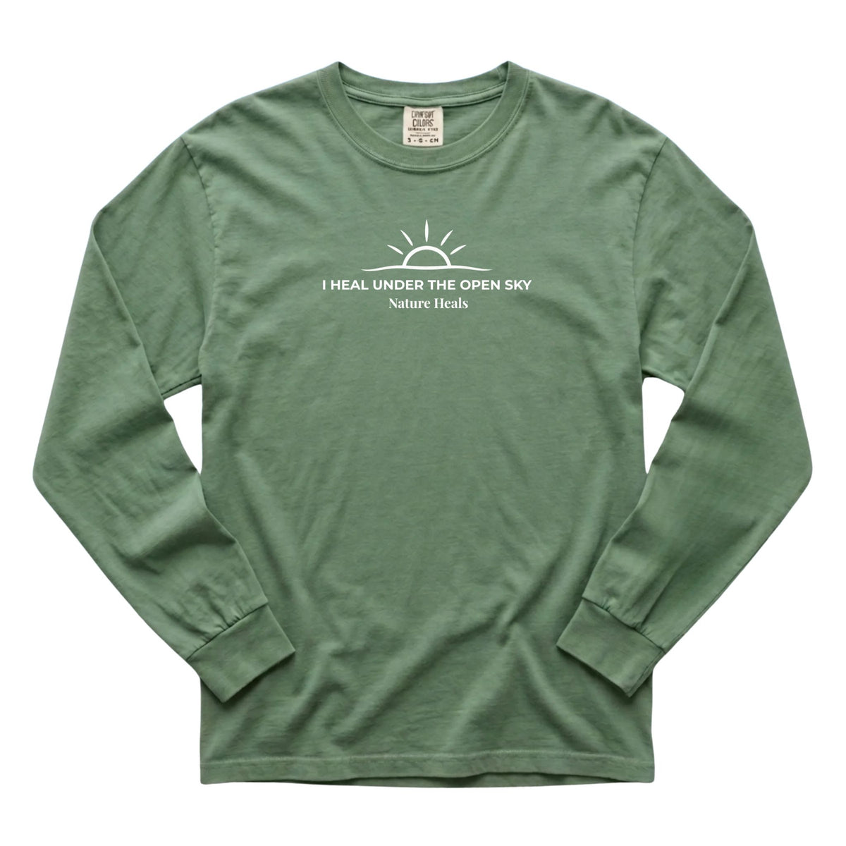 A light green long-sleeve t-shirt with a white graphic on the chest featuring a sun and the text 'I HEAL UNDER THE OPEN SKY' and 'Nature Heals'.
