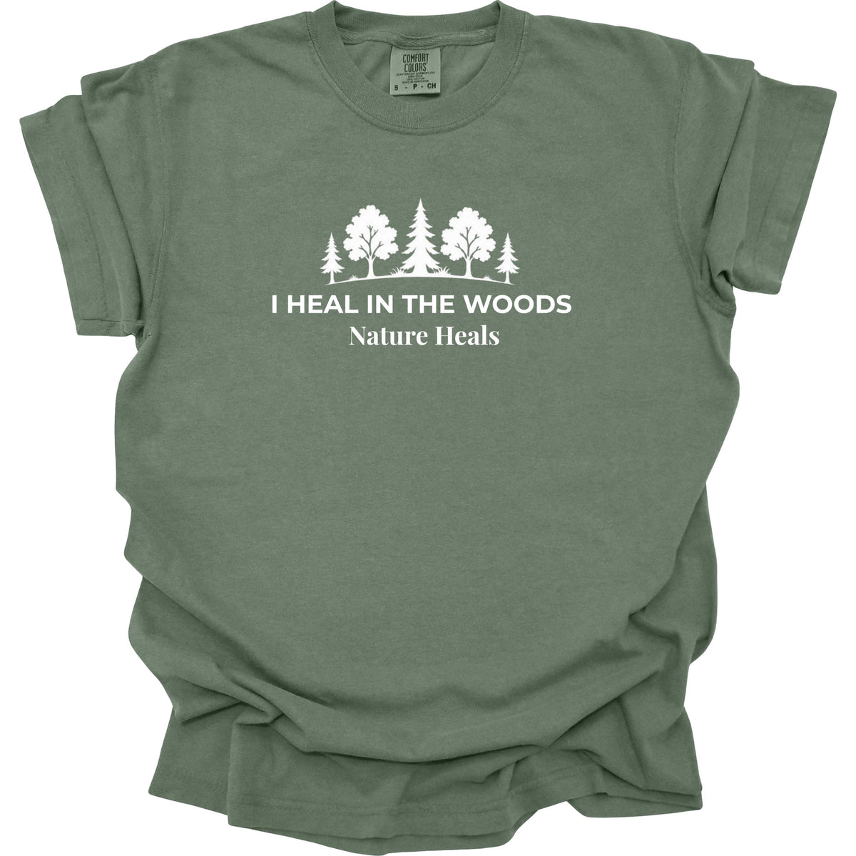 An moss green crewneck t-shirt with a white graphic of trees and the text 'I HEAL IN THE WOODS Nature Heals' printed on the chest, displayed flat against a white background.