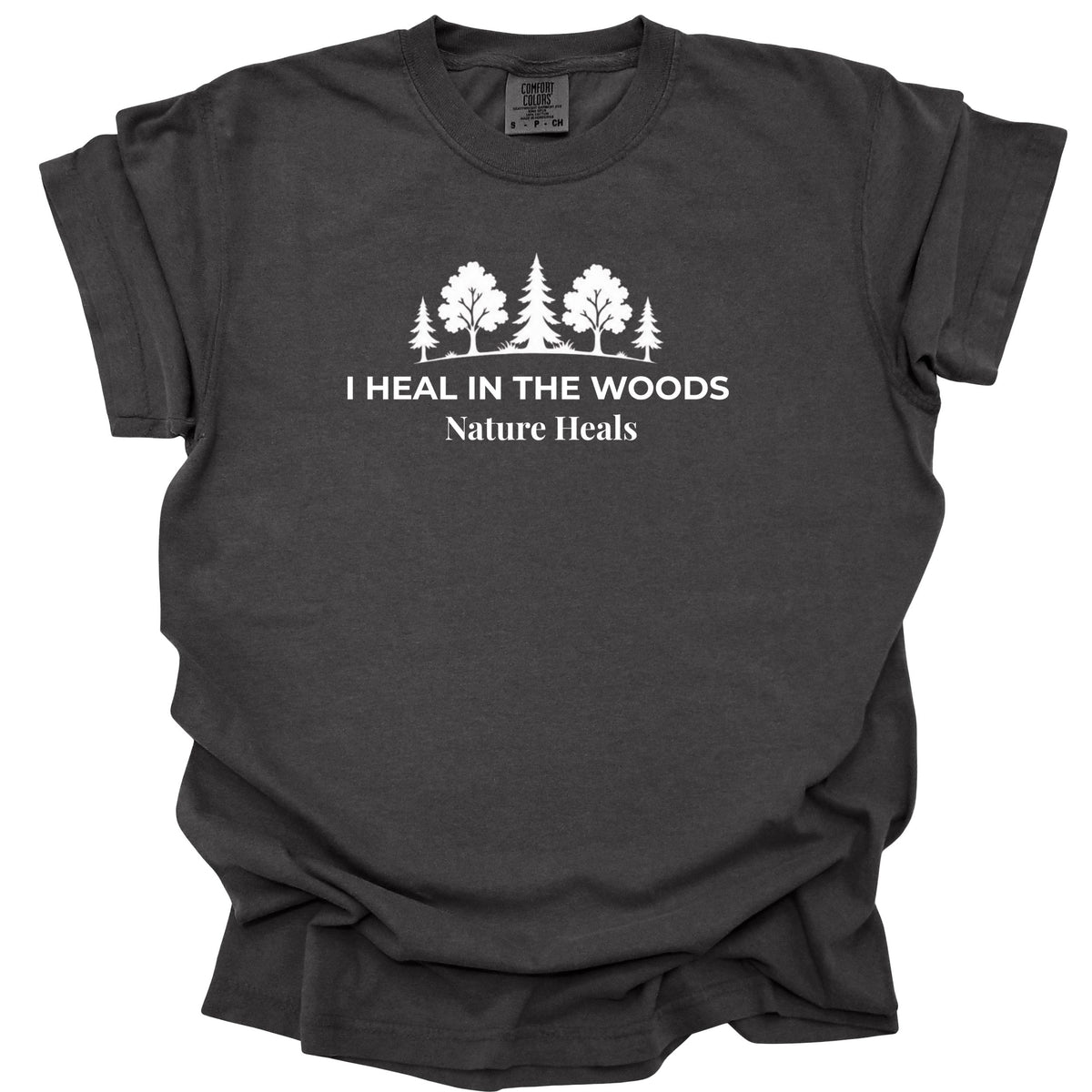 A dark charcoal gray t-shirt with a white graphic print of trees and the text 'I HEAL IN THE WOODS Nature Heals' on the chest, displayed against a solid white background.