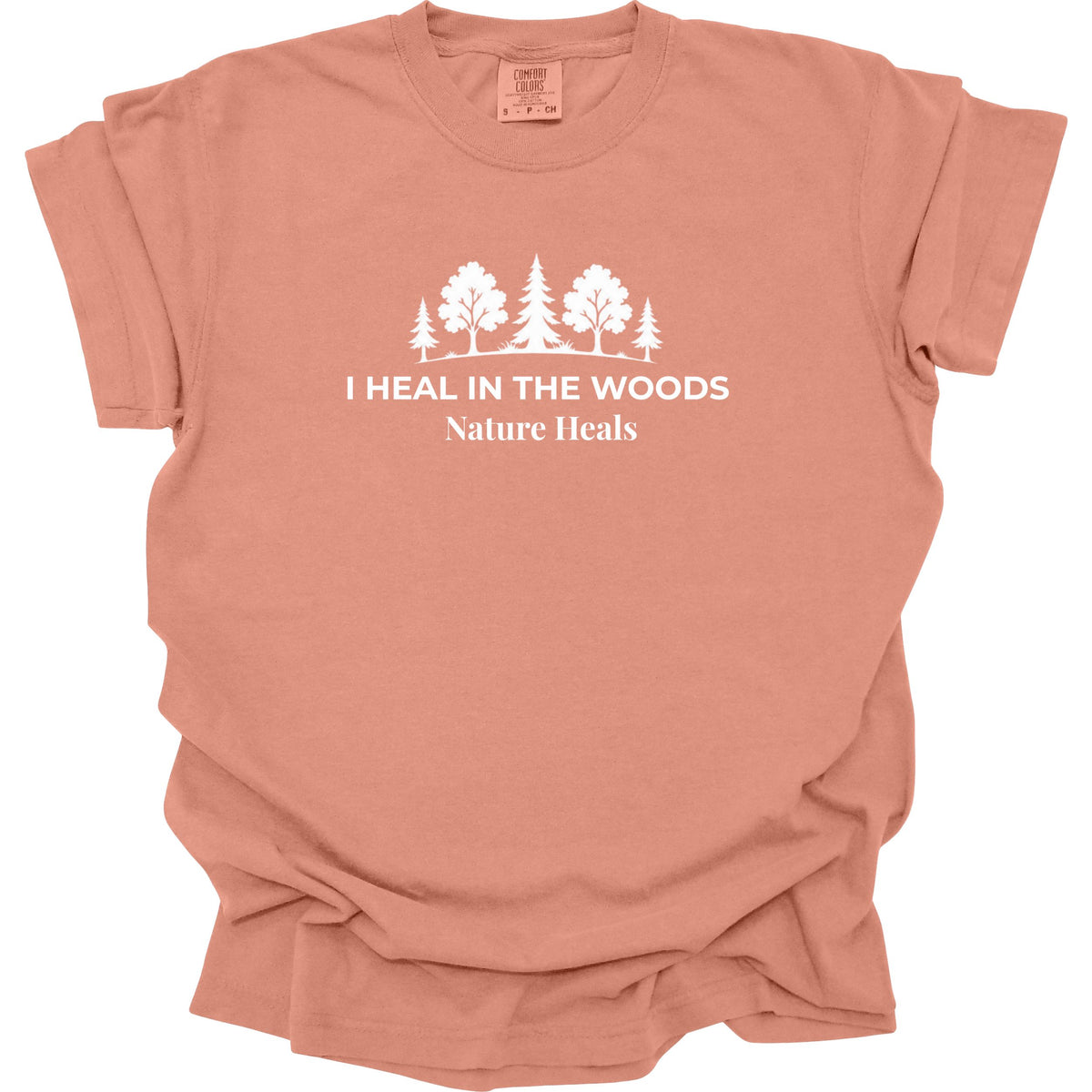 A terracotta-colored short-sleeve t-shirt with a white graphic of trees and the text 'I HEAL IN THE WOODS Nature Heals' printed on the chest, shown against a plain white background.