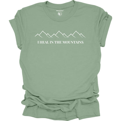 Sage green t-shirt with mountain graphic and text 'I Heal in the Mountains' on a white background
