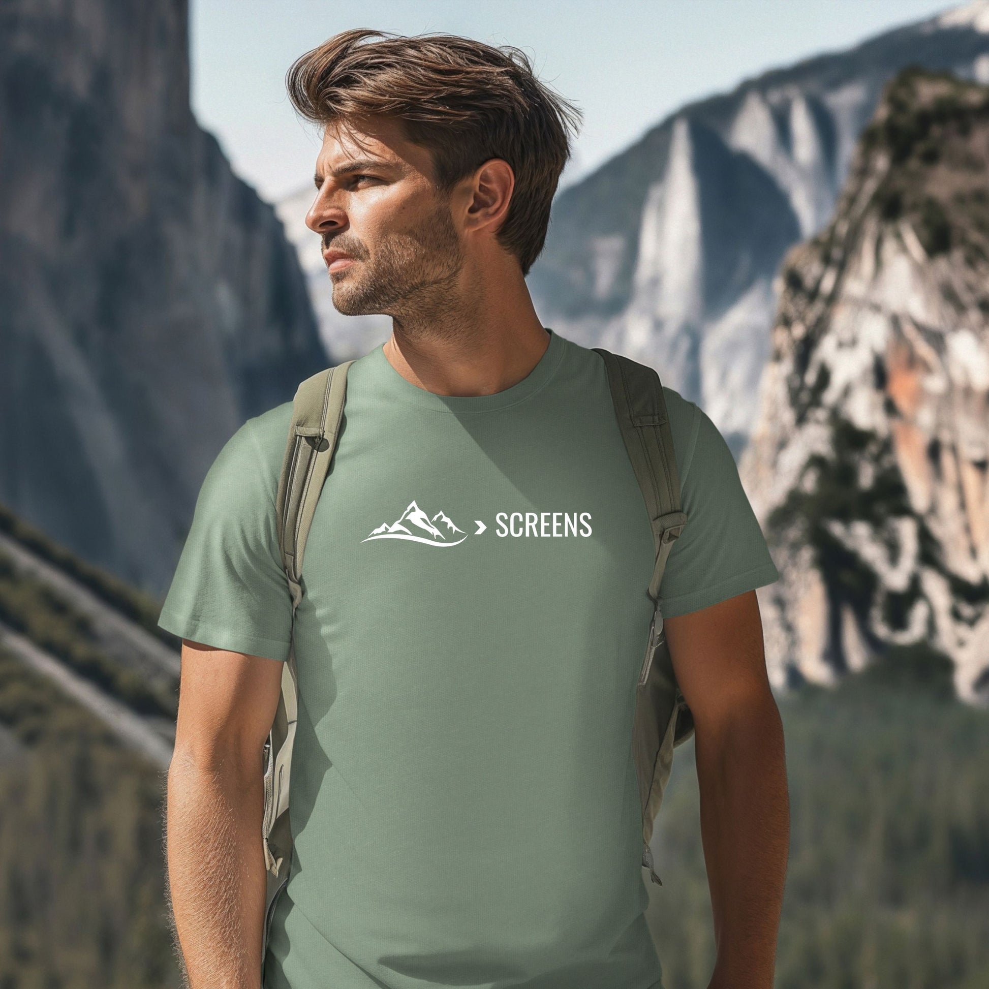 Man wearing a green t-shirt with a mountain graphic  and text that says > SCREENS, standing in front of mountains.