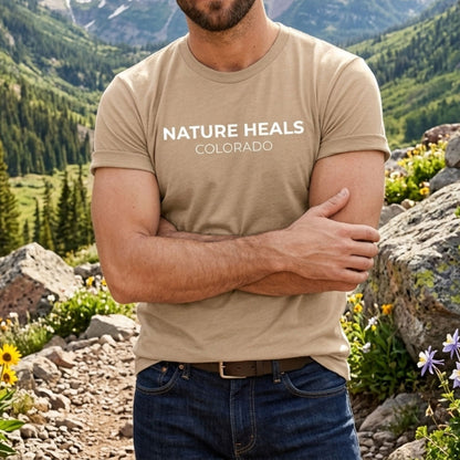 Man wearing a tan 'Nature Heals Colorado' t-shirt in a mountainous landscape.