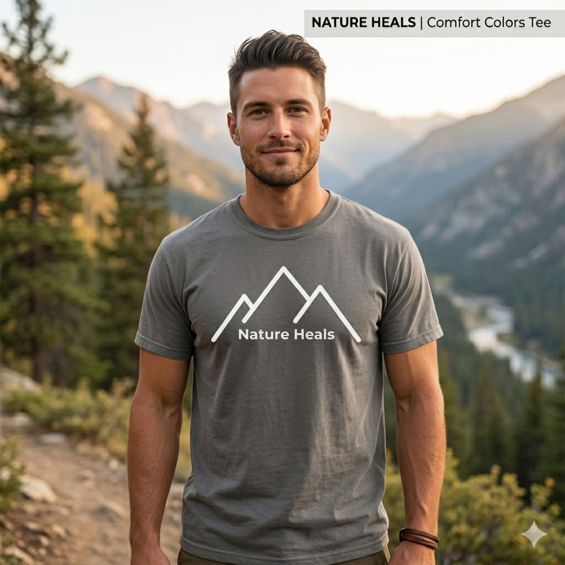 Man wearing a 'Nature Heals' grey t-shirt with white mountain graphic  mountains in the background