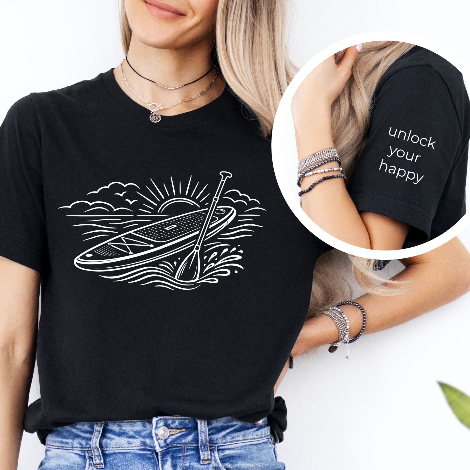 Black t-shirt featuring white line art of a stand up paddle board with paddle on water at sunrise, worn by model, ocean and beach lifestyle design