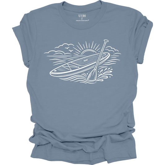 Blue t-shirt featuring white line art of a stand up paddle board with paddle on water at sunrise, worn by model, ocean and beach lifestyle design