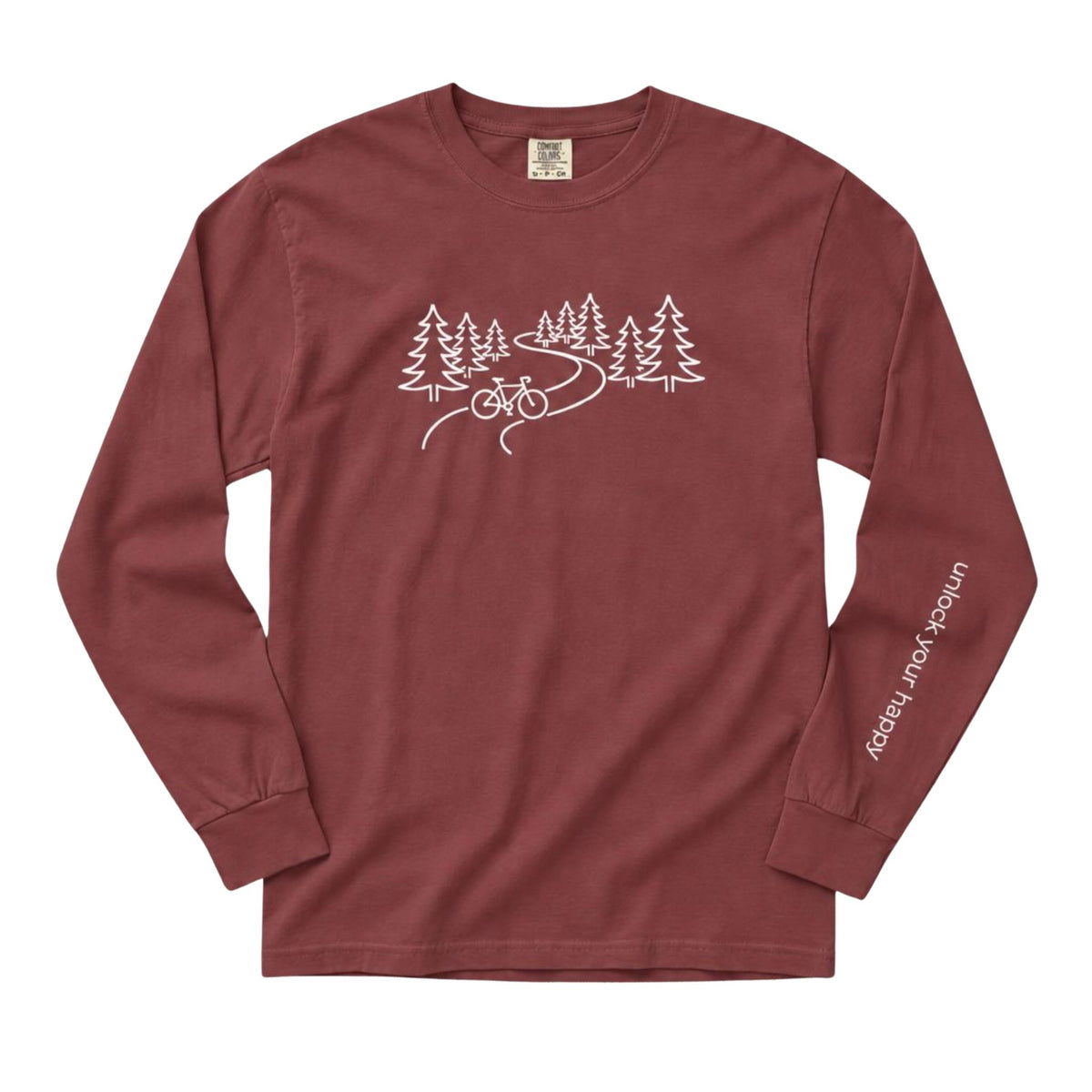 A long-sleeve crewneck t-shirt in a dusty brick red color, featuring a white line art graphic of pine trees, a winding road, and a bicycle on the chest, with 'Unlock Your Happy' printed vertically in white on the left sleeve.