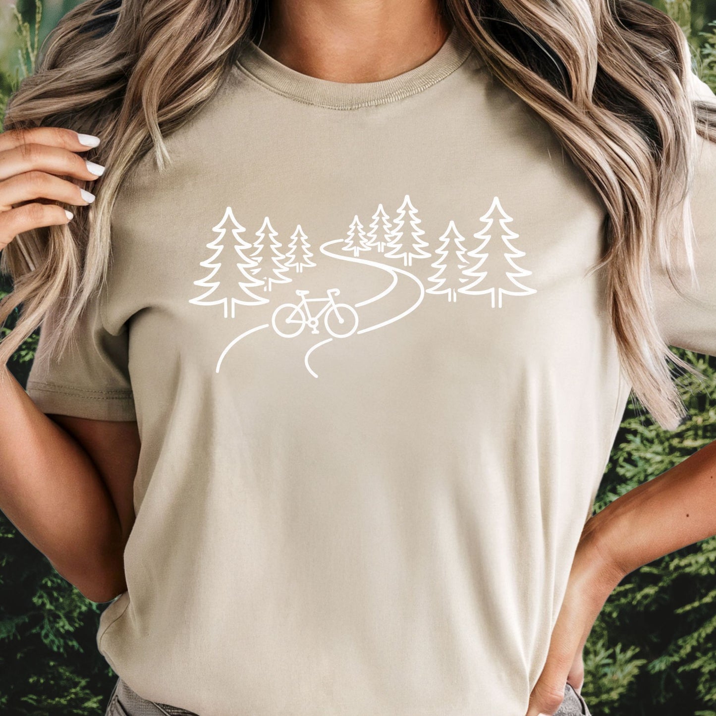 nature biking tan graphic t-shirt with minimalist forest trail and bicycle design, featuring “unlock your happy” text on sleeve on female outdoors