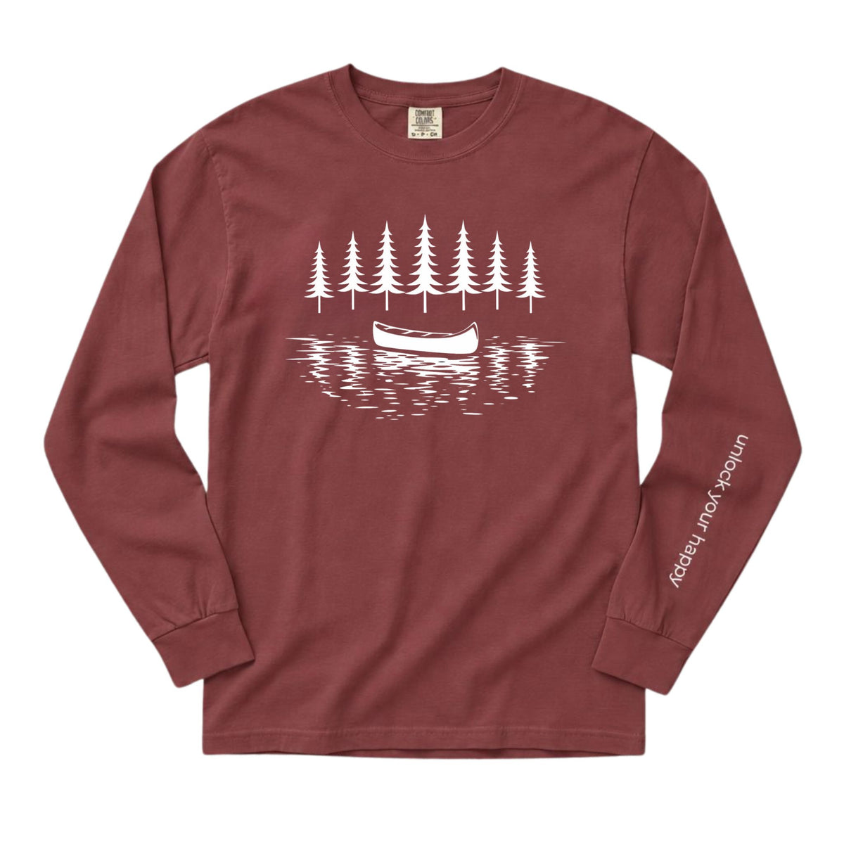 A long-sleeve crewneck t-shirt in a brick red color, featuring a white graphic print of pine trees, a canoe, and water on the chest, with white text on the left sleeve reading 'unlock your happy'.