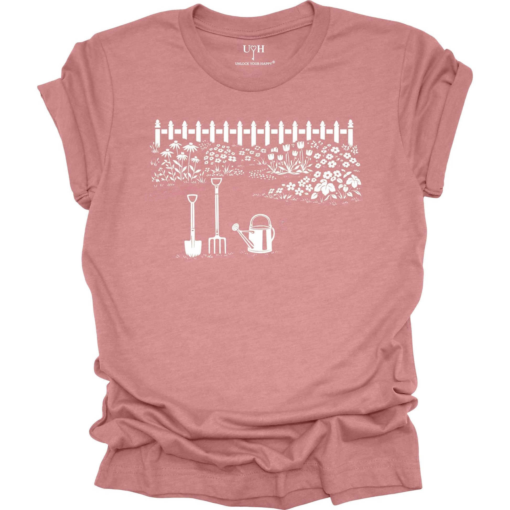 White gardening graphic on a mauve t-shirt featuring garden tools and flower garden illustration with nature-inspired design 