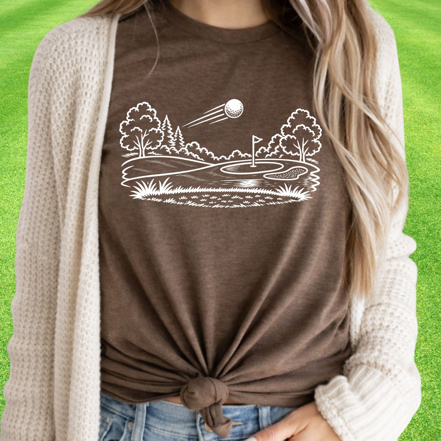 Minimalist golf course graphic t-shirt with line art design of golf ball and green on soft unisex brown tee on green lawn