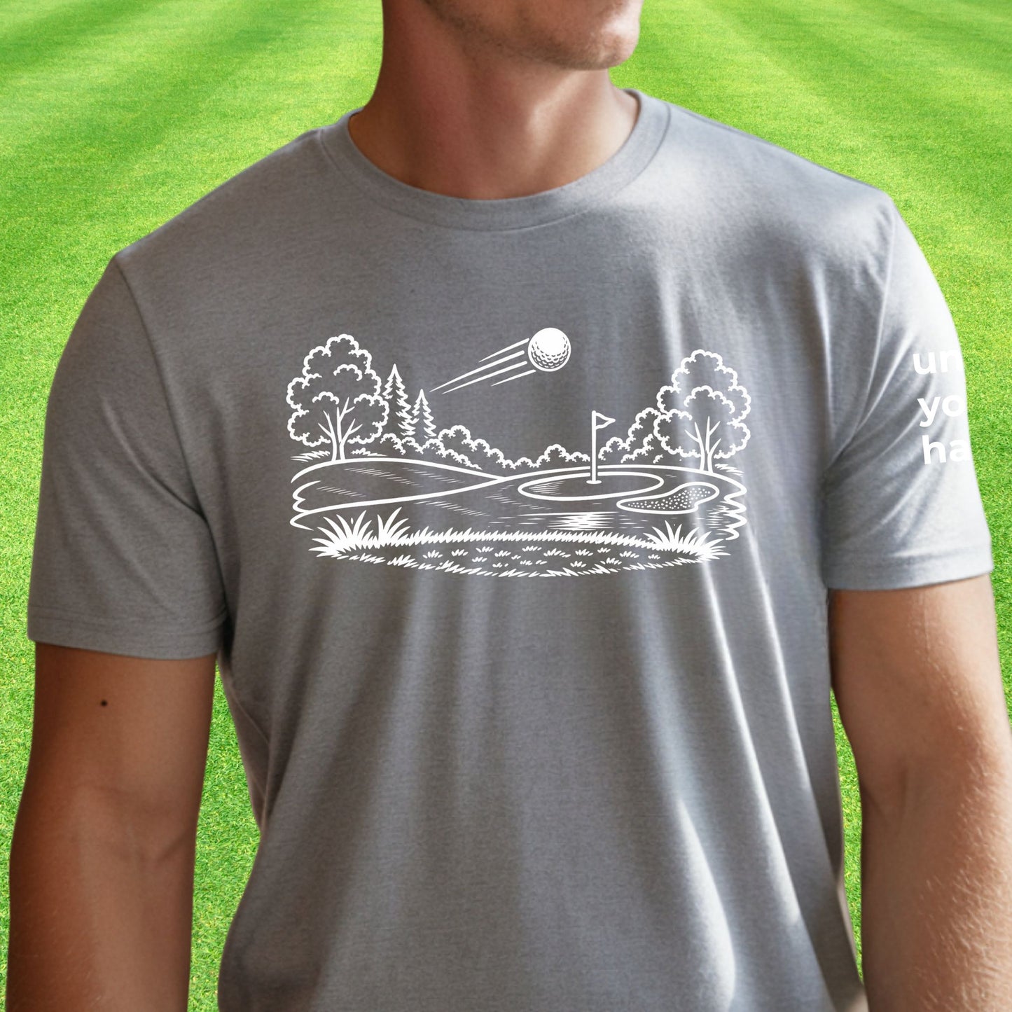 Minimalist golf course graphic t-shirt with line art design of golf ball and green on soft unisex gray tee on green lawn