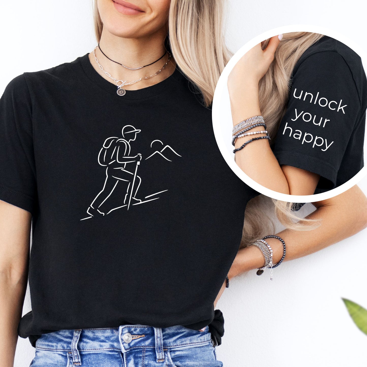 Person wearing a black t-shirt with hiking graphic and mountain and text unlock your happy on the sleeve