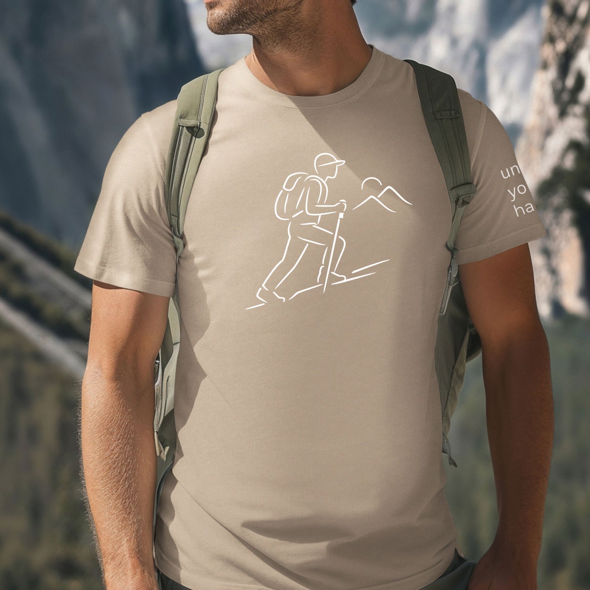 man wearing a tan t-shirt with hiking graphic and mountains with mountain background
