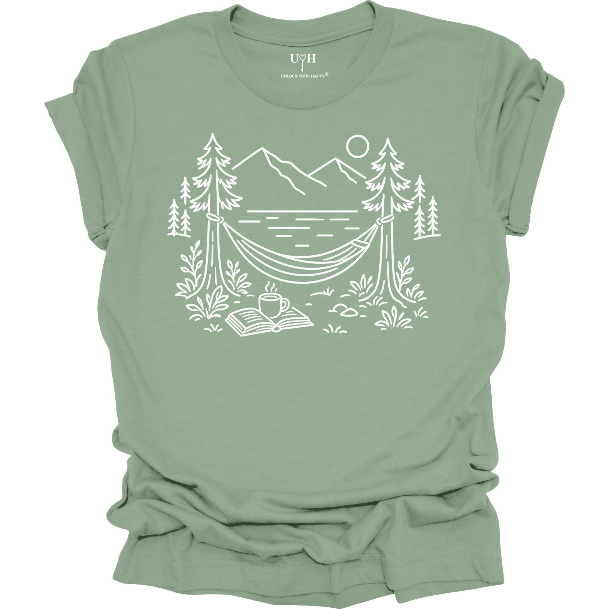Sage unisex t-shirt with a white line art hammock scene featuring mountains, trees, a lake, coffee cup, and open book, plus ‘unlock your happy’ on the sleeve.