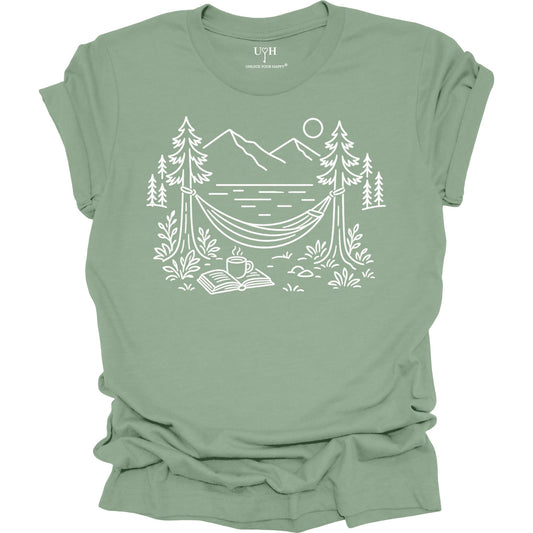 Sage unisex t-shirt with a white line art hammock scene featuring mountains, trees, a lake, coffee cup, and open book, plus ‘unlock your happy’ on the sleeve.