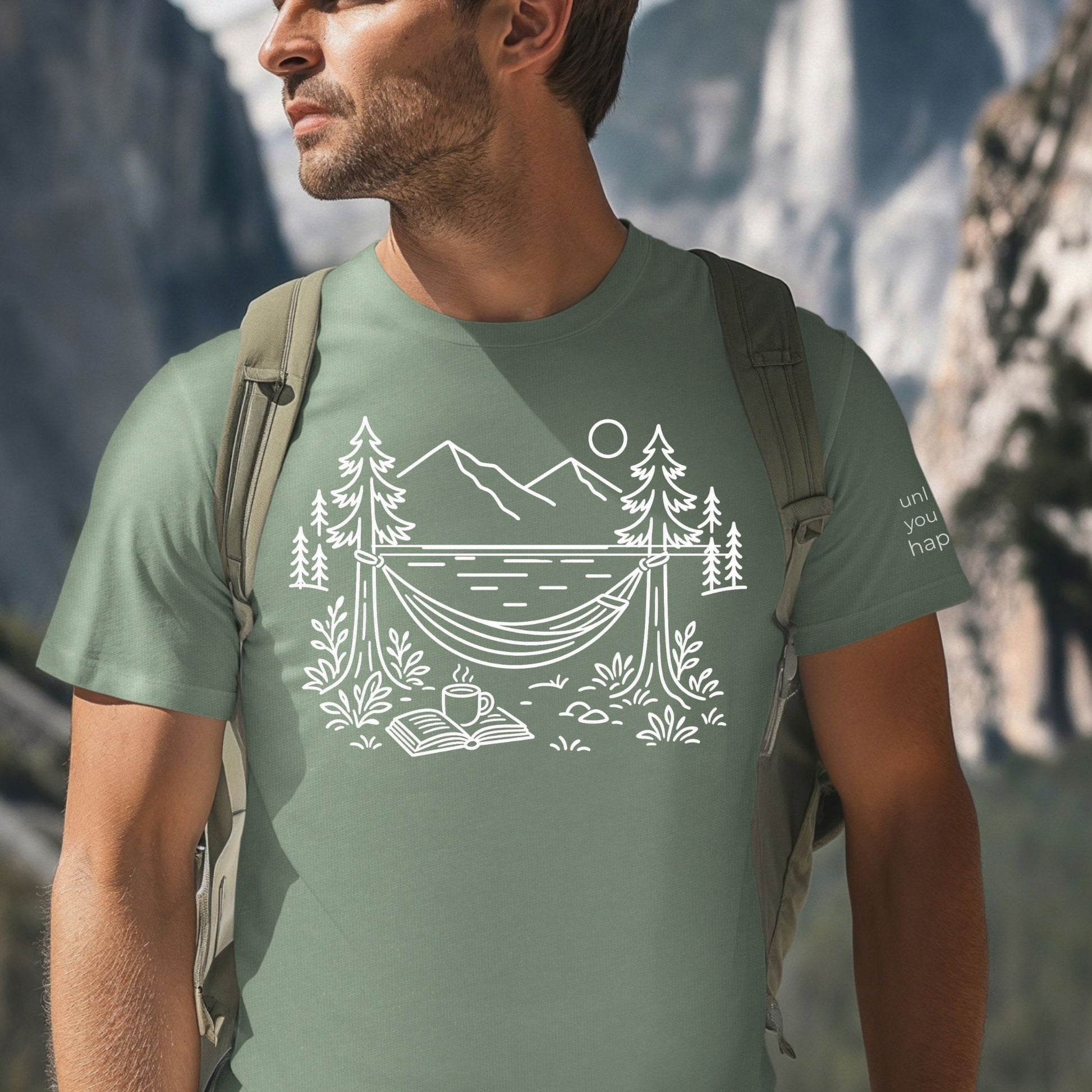 Sage  unisex t-shirt with a white line art hammock scene featuring mountains, trees, a lake, coffee cup, and open book, plus ‘unlock your happy’ on the sleeve on a male.