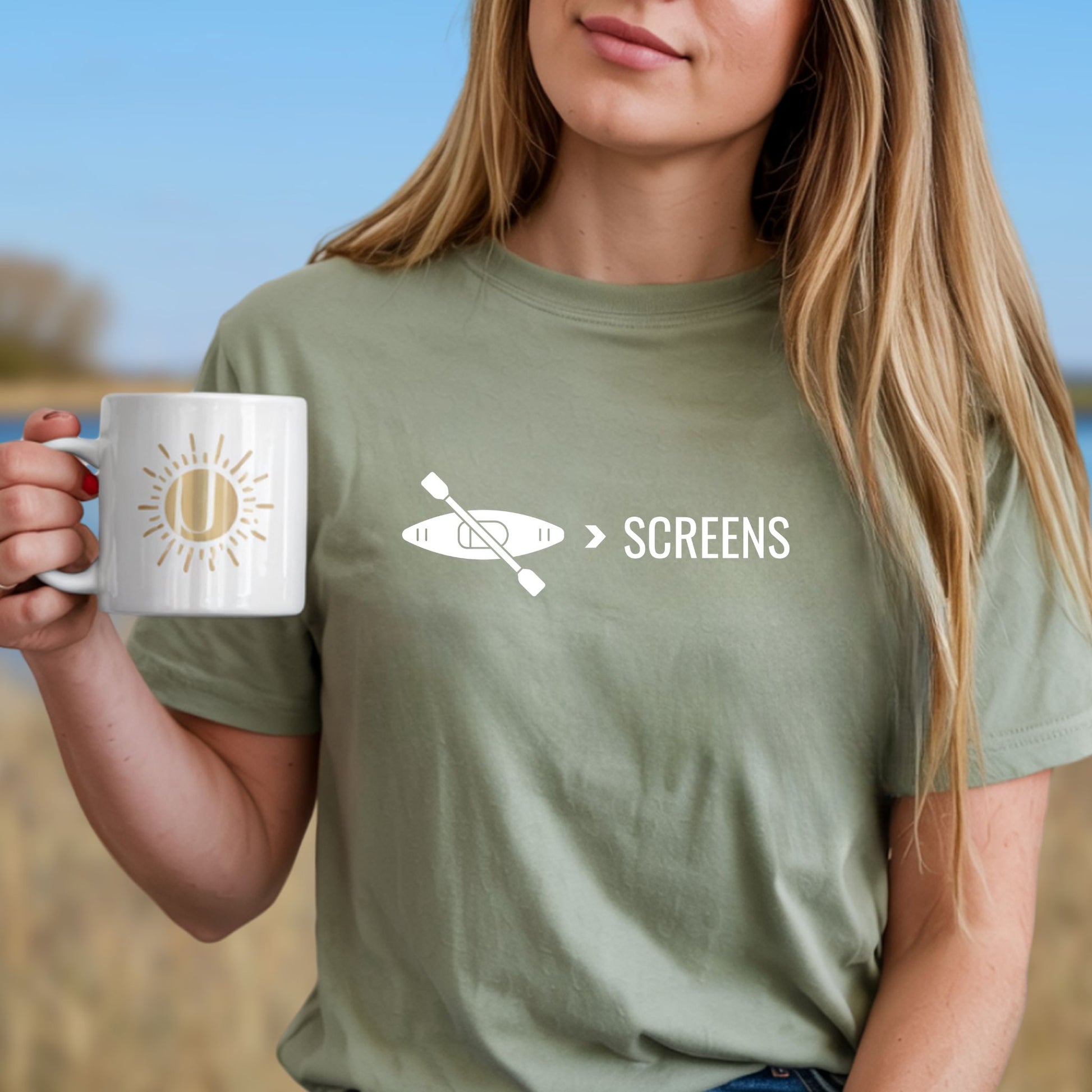 Woman outside wearing a sage green  t-shirt with Kayak over screens  text with paddle graphic, digital detox nature shirt for outdoor lovers
