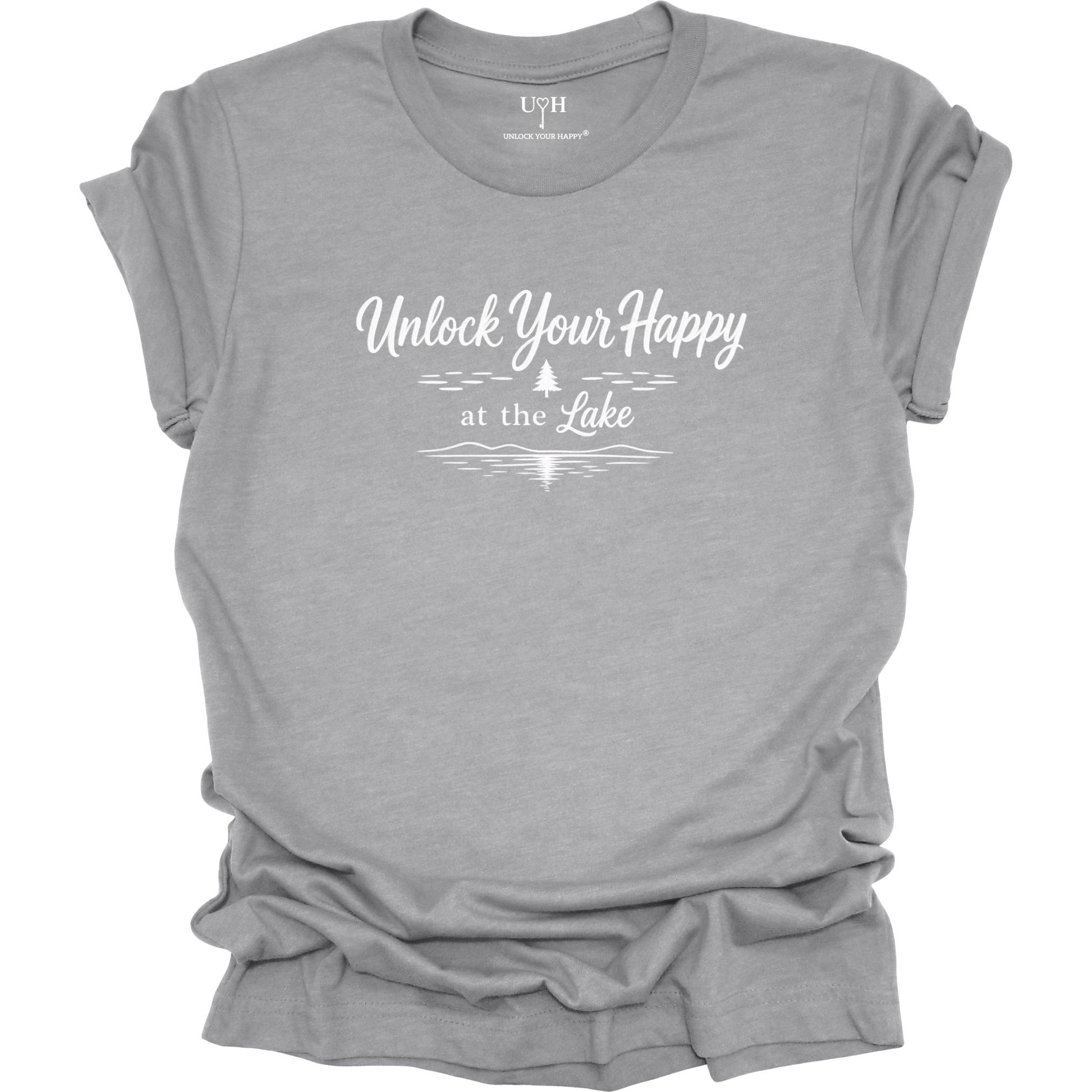 Gray t-shirt with 'Unlock Your Happy by the Lake' text and a simple pine tree and lake wave graphic on a white background