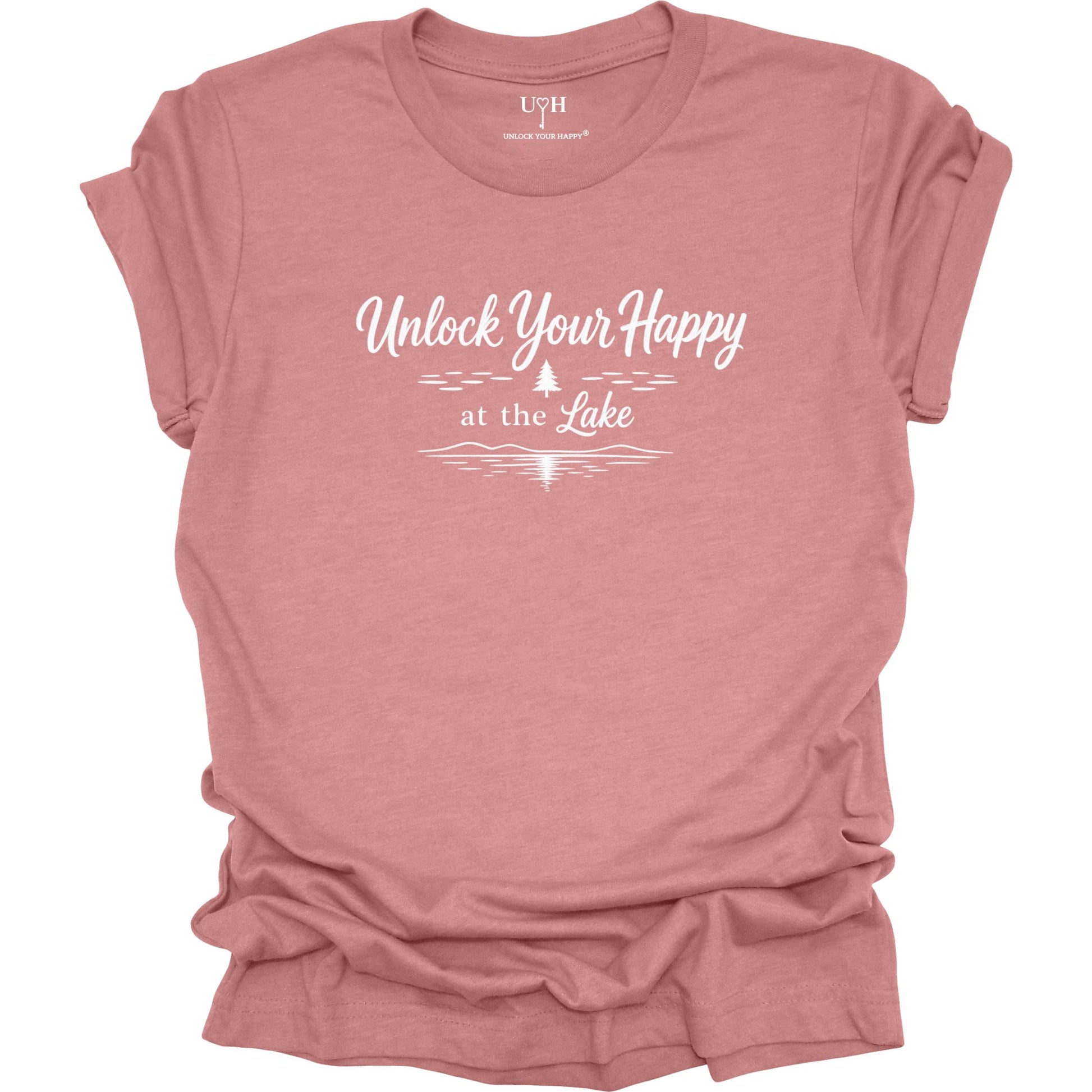 A mauve short-sleeve t-shirt with a white graphic print that reads 'Unlock Your Happy at the Lake' above a simple pine tree line and lake wave, shown on a plain white background.