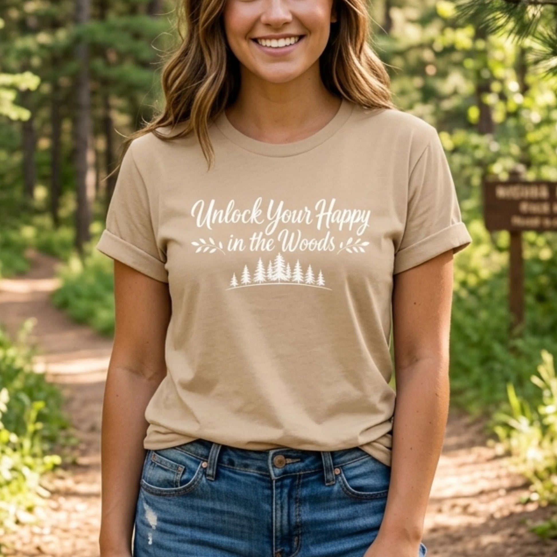 Unlock Your Happy in the Woods White Text with tree line on a tan t-shirt on a female in the woods