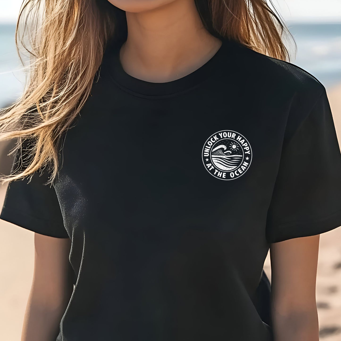Female wearing a left chest ocean graphic black t-shirt with 'Unlock Your Happy' text on the beach