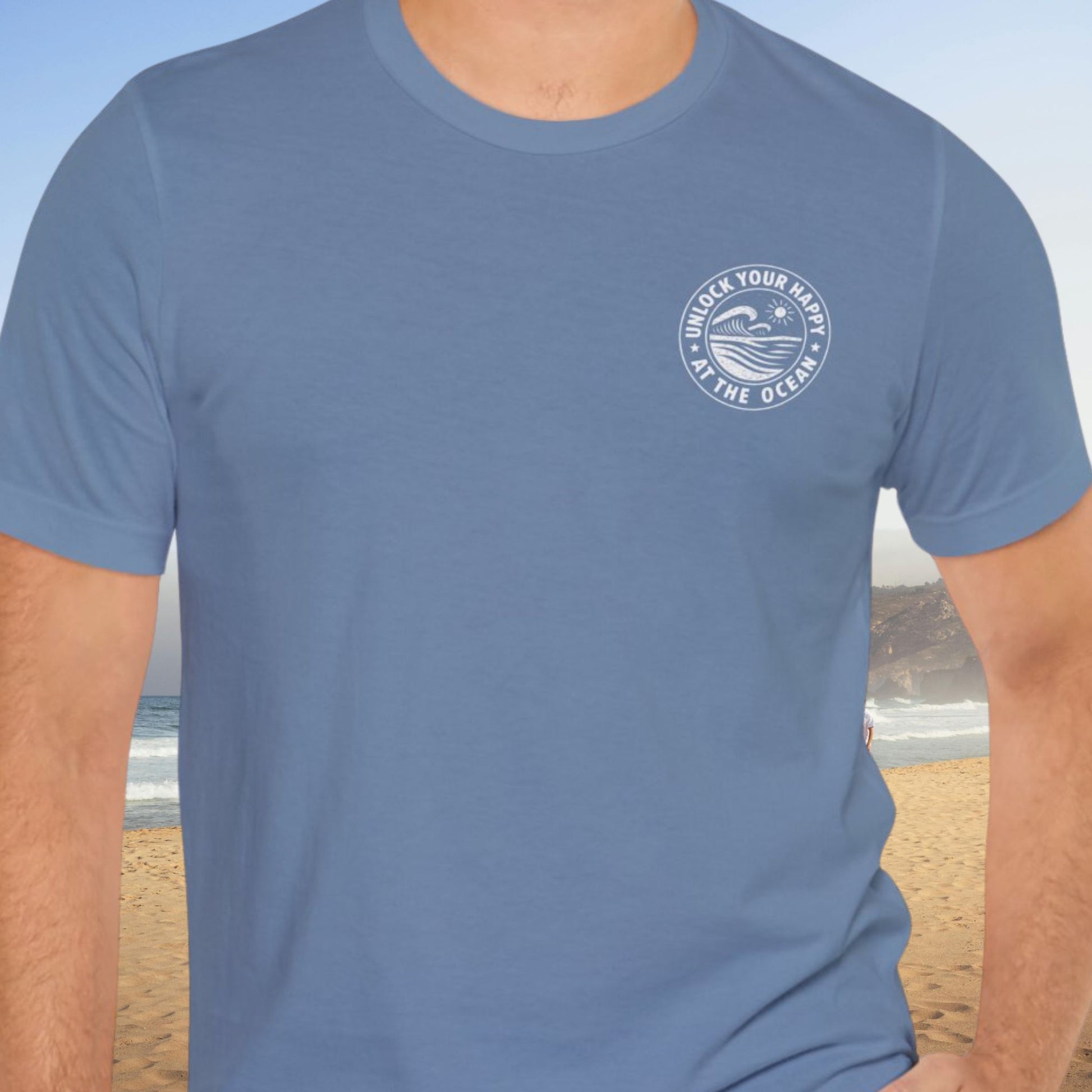 Male wearing a left chest ocean graphic blue t-shirt with 'Unlock Your Happy' text on the beach