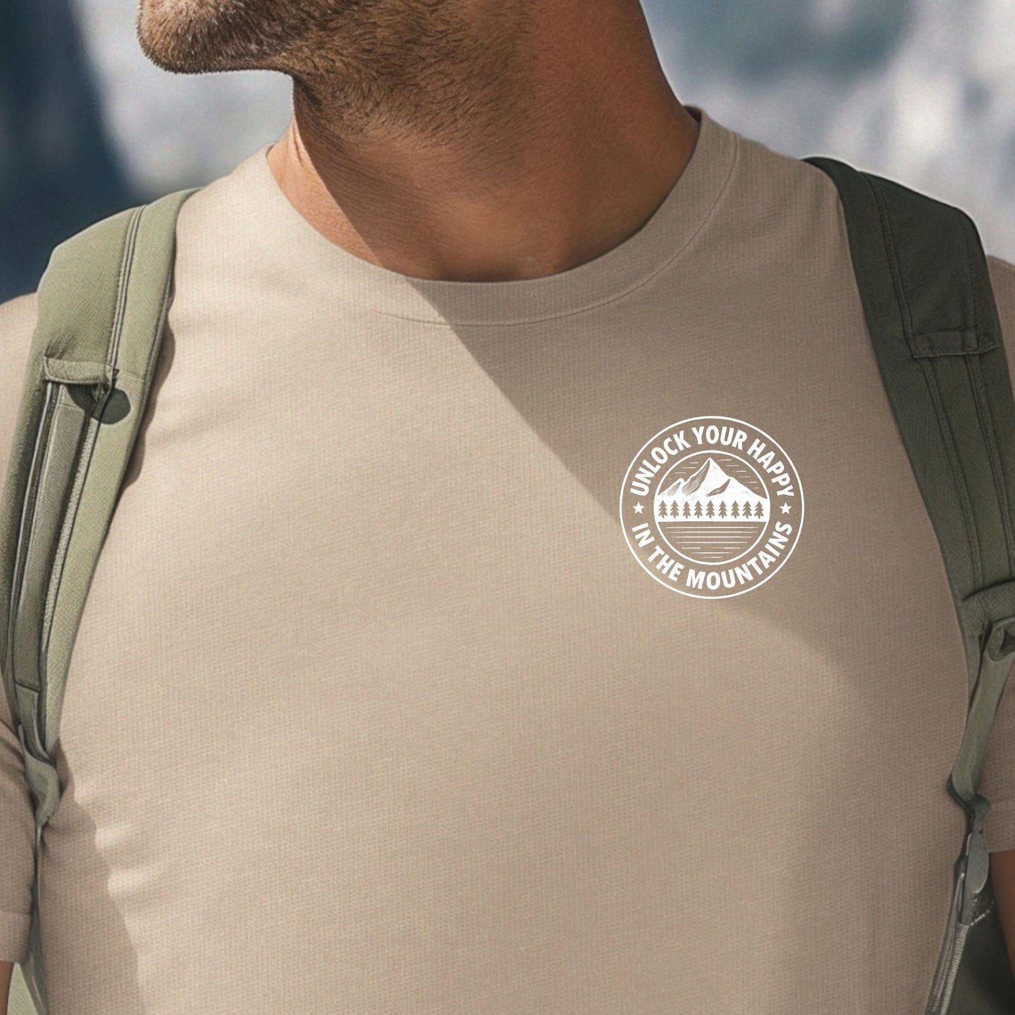 Male wearing a left chest mountain graphic tan t-shirt with 'Unlock Your Happy' text  