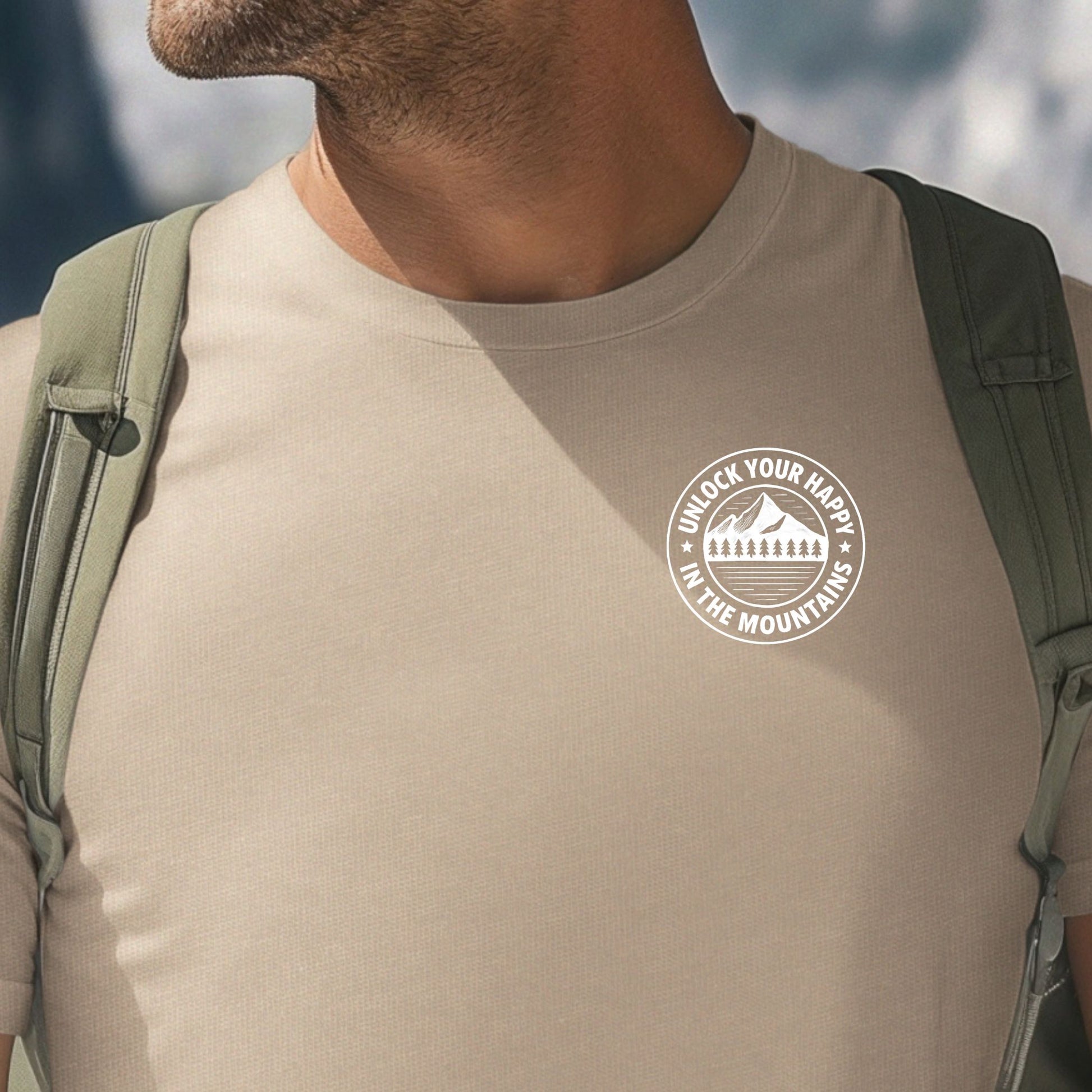 Male wearing a left chest mountain graphic tan t-shirt with 'Unlock Your Happy' text  