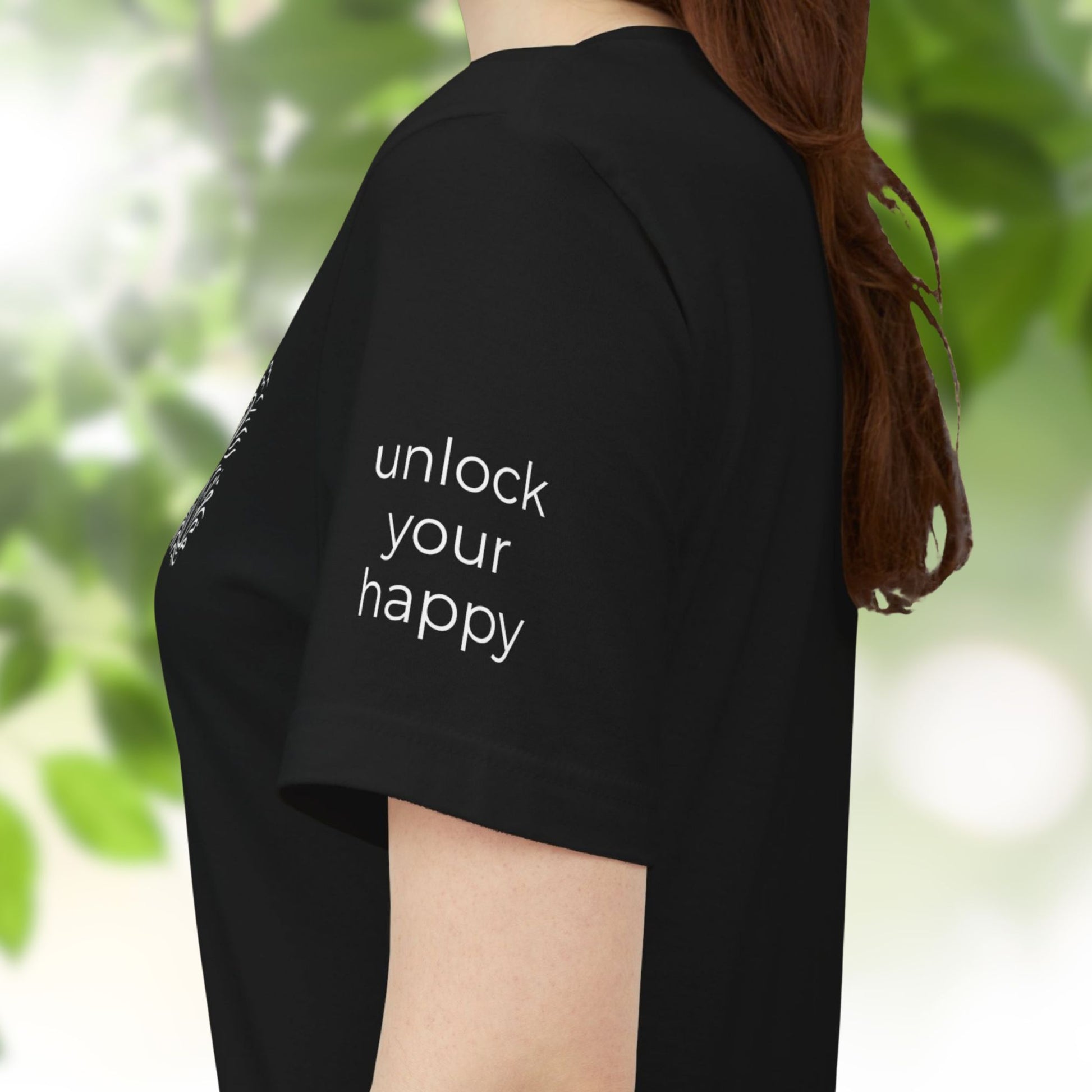 Person wearing a black t-shirt with 'unlock your happy' text on the sleeve, standing in a natural setting.