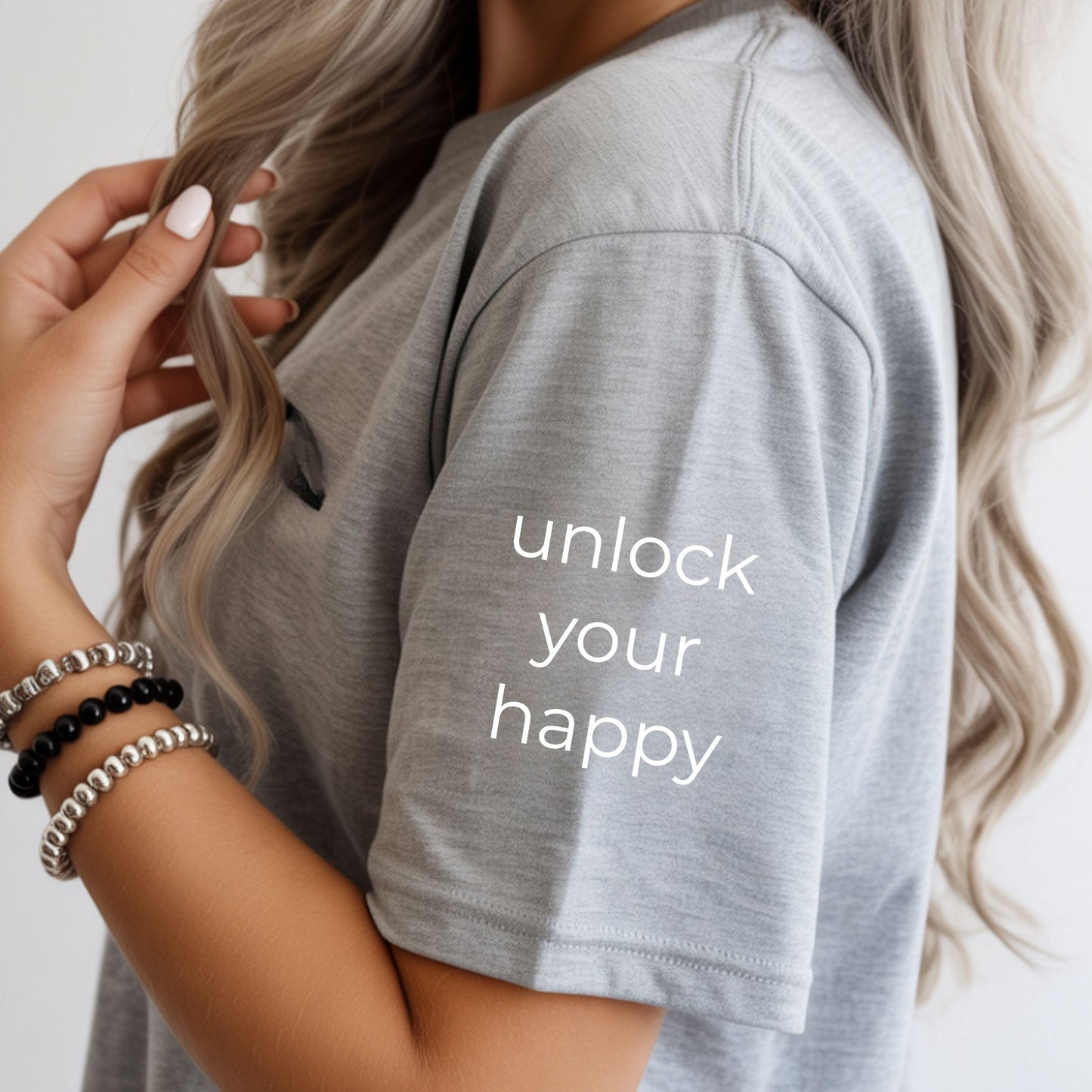 Person wearing a gray t-shirt with 'unlock your happy' text, holding hair.